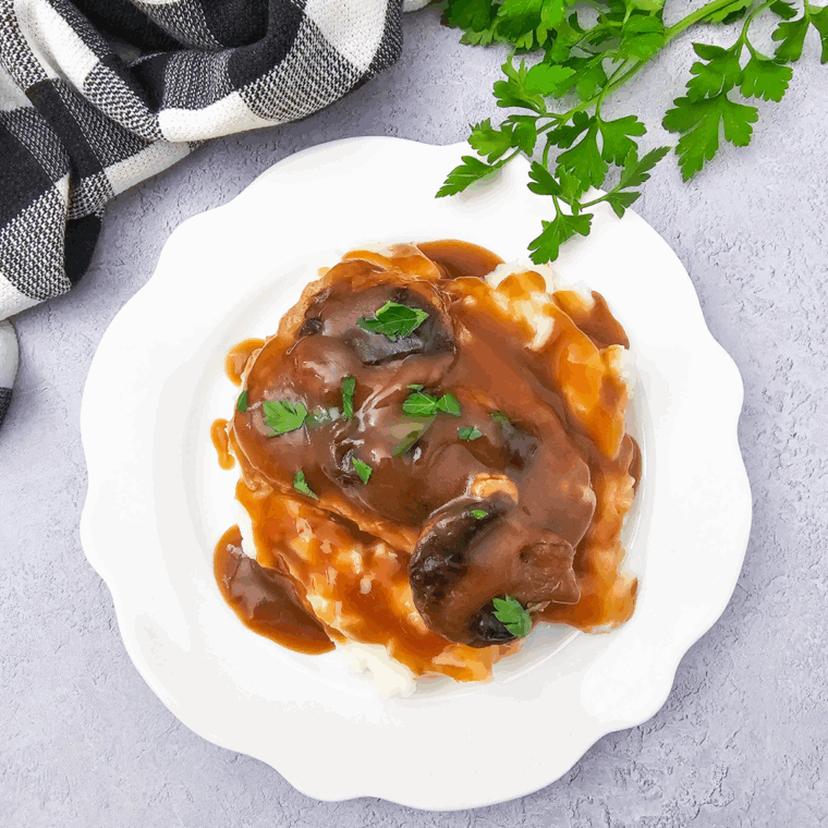 Tender pork chops cooking in crockpot with brown gravy and mushrooms