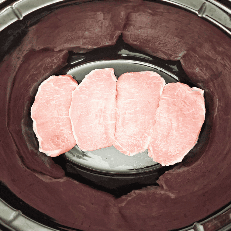 Boneless pork chops placed in the bottom of a crockpot.