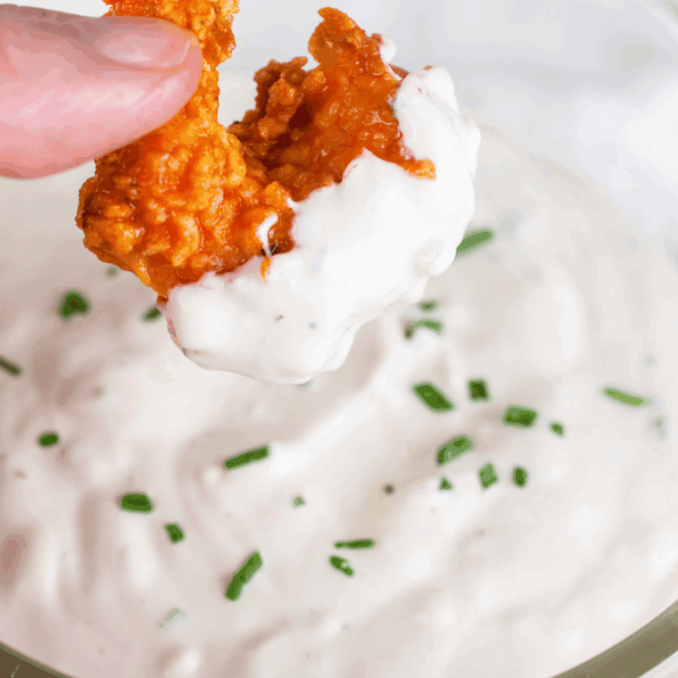 Small bowl of creamy blue cheese dressing with crumbled blue cheese and celery sticks on the side.