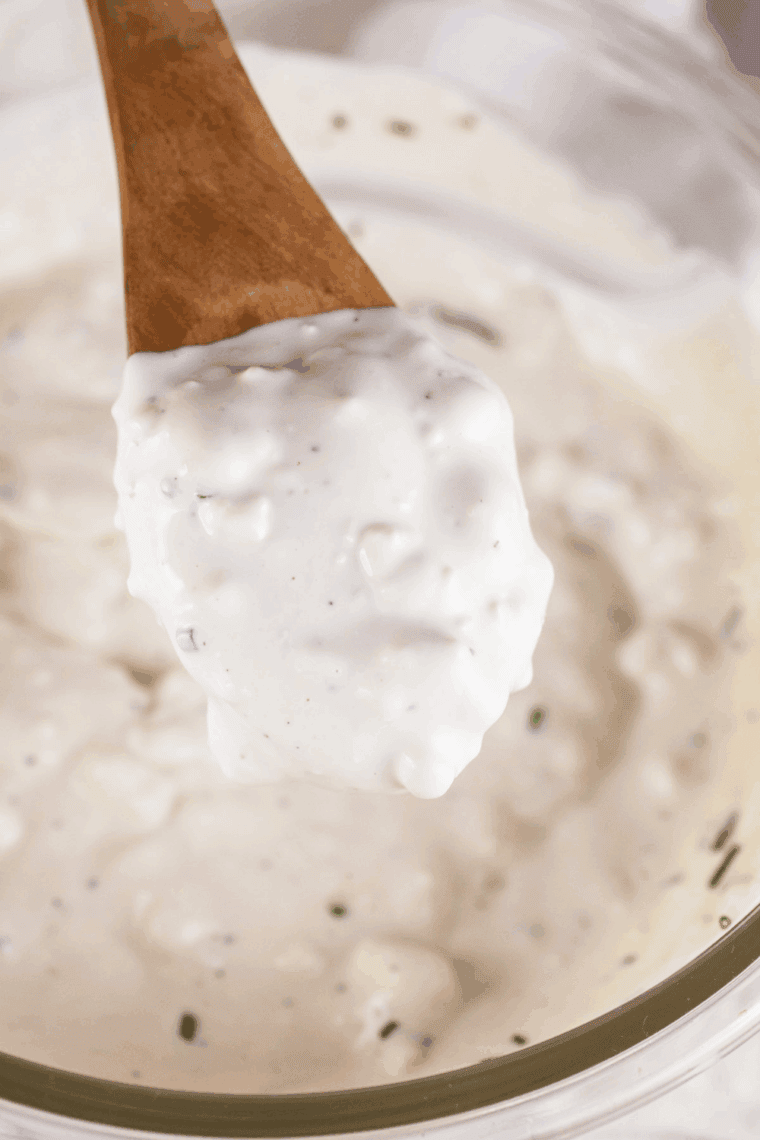 Homemade blue cheese dressing in a small bowl, topped with crumbles of blue cheese, served with celery and chicken wings.