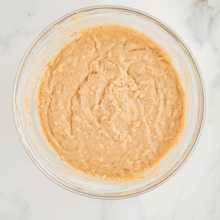 Wet ingredients being whisked together with mashed bananas in a large bowl.