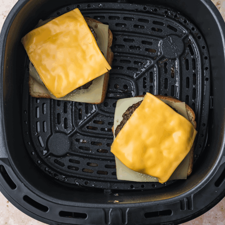 Cooked burger in the air fryer basket with cheese on top.