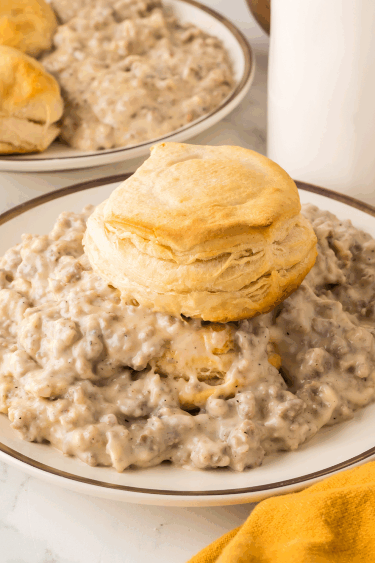 Plate of sausage gravy with biscuits on top.
