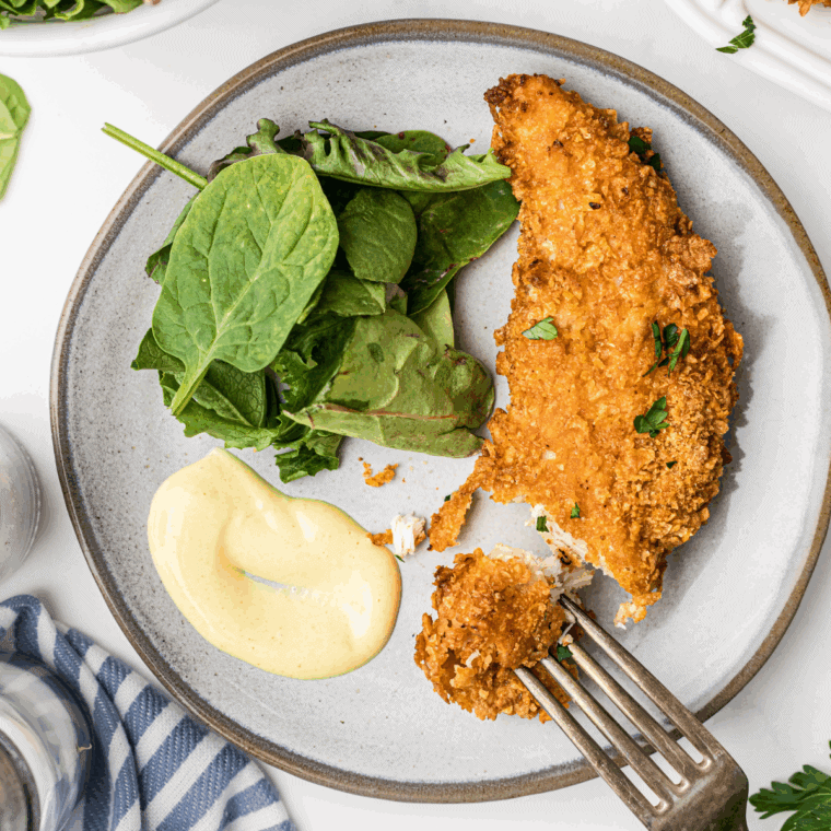 A bowl of homemade Hardee's honey mustard sauce with spoon and chicken tender.