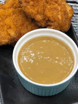 Small bowl of creamy Jack In The Box honey mustard sauce with a dipping spoon and chicken tenders on the side.