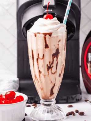 Glass of homemade Ninja Creami McDonald’s chocolate milkshake topped with whipped cream and a cherry.