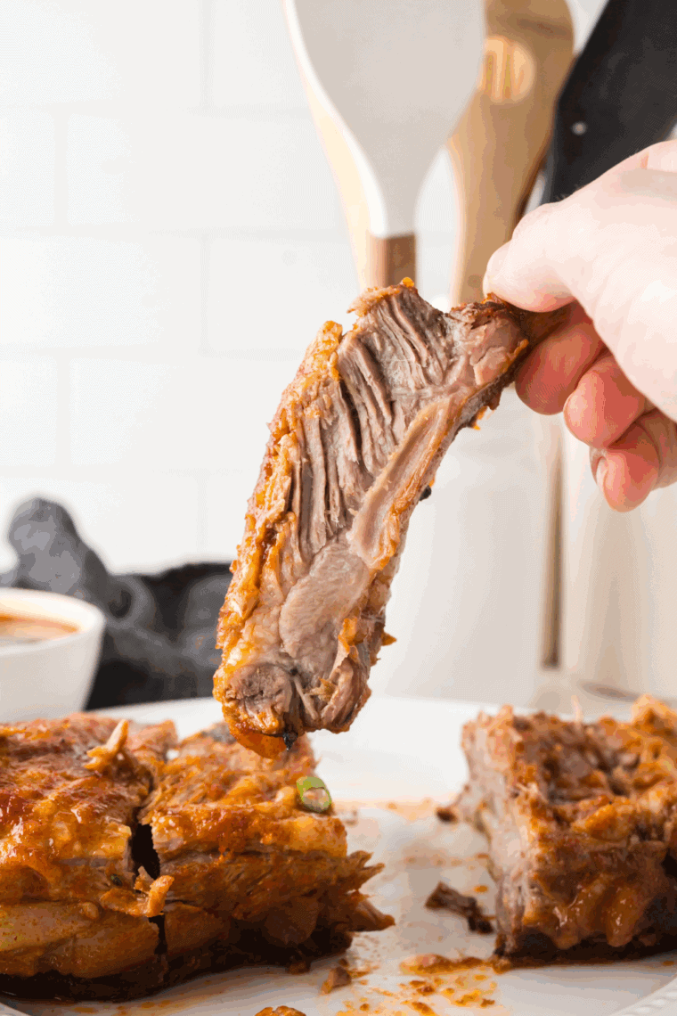 Cooked juicy ribs being held in the air showing the meaty texture. Tender, fall off the bone ribs.