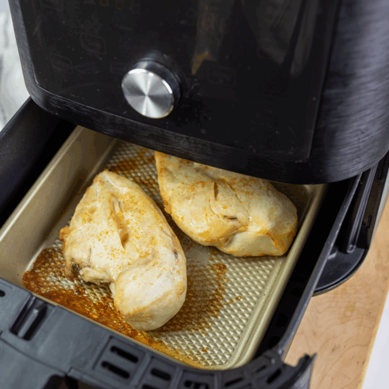 Seasoned chicken in the air fryer basket.