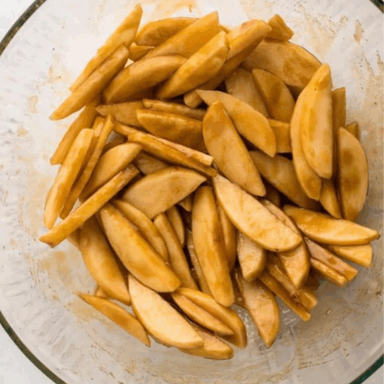 Peeled and sliced apples tossed in butter, brown sugar, and cinnamon in a mixing bowl.