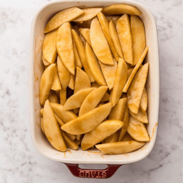 Coated apple slices arranged in a baking dish inside the air fryer basket.