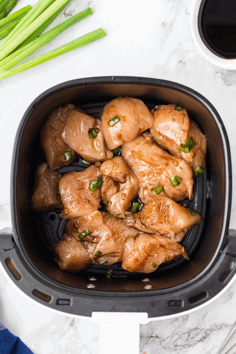 Chicken thighs cooking in a single layer in an air fryer basket.