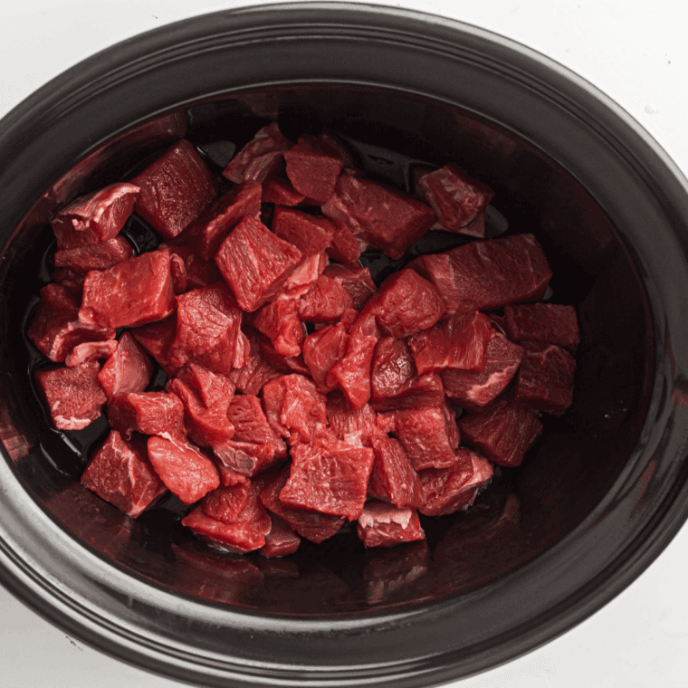 Raw beef cubes and chopped onion layered in a slow cooker.