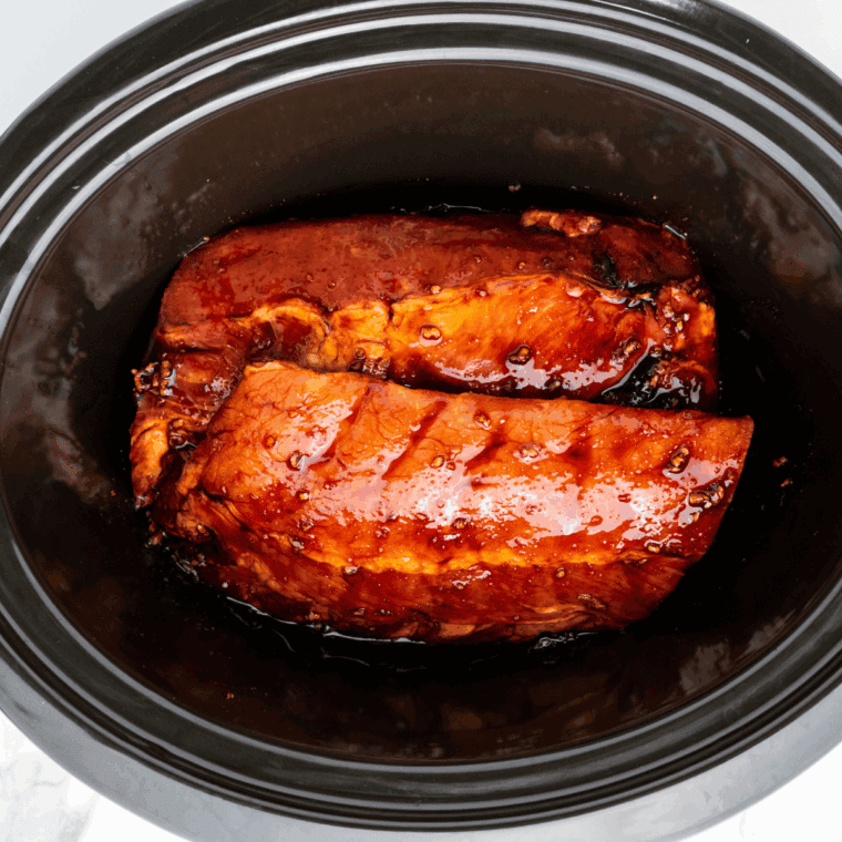 Ribs in slow cooker with Dr. Pepper and BBQ sauce being brushed on top.