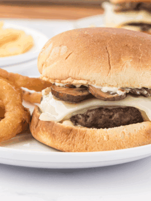 Bowl of creamy Smashburger-style sauce with a spoon, surrounded by burger fixings.