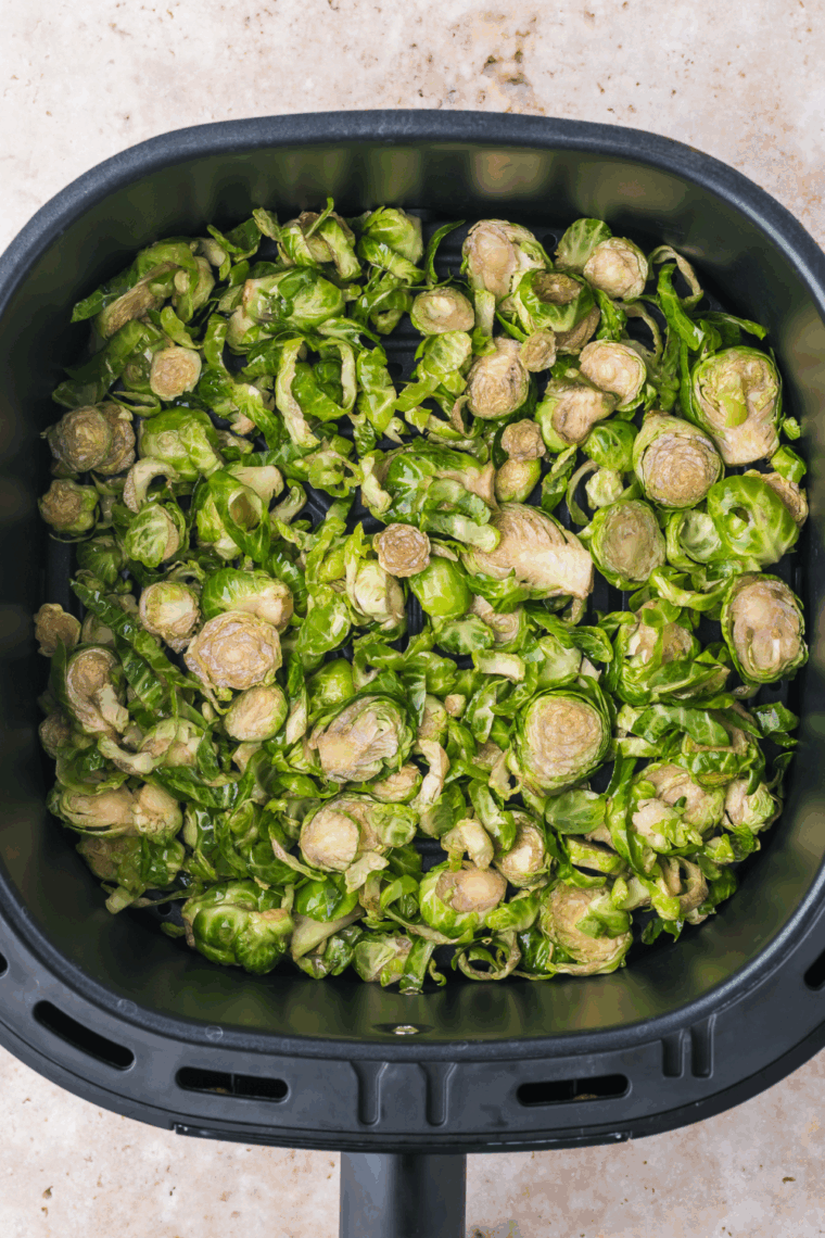 Shaved Brussels sprouts air frying in a single layer until golden and crispy.