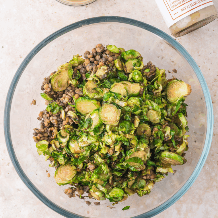 Tossing crispy Brussels sprouts with lentils and sesame dressing in a large bowl for a warm, flavorful salad.
