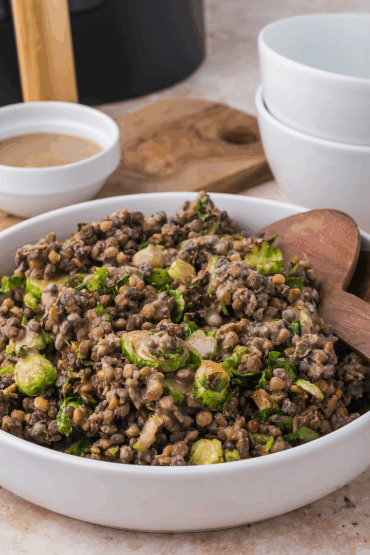 Air fryer roasted Brussels sprouts mixed with steamed lentils and tossed in Trader Joe’s Organic Toasted Sesame Dressing in a large bowl.