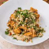 Bowl filled with Trader Joe’s Shawarma Chicken, hummus, and cauliflower tabbouleh, served with fresh vegetables.