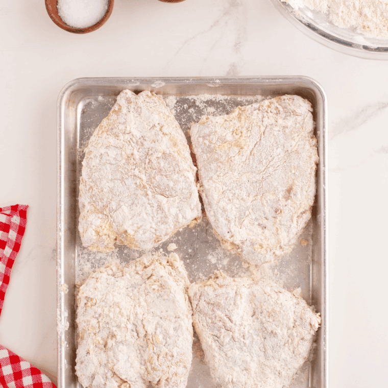 Breaded chicken on a baking sheet, ready to be battered.