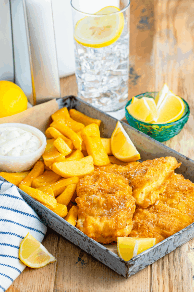 Plate of golden, crispy Arthur Treacher’s style fish and chips with lemon wedges and tartar sauce.