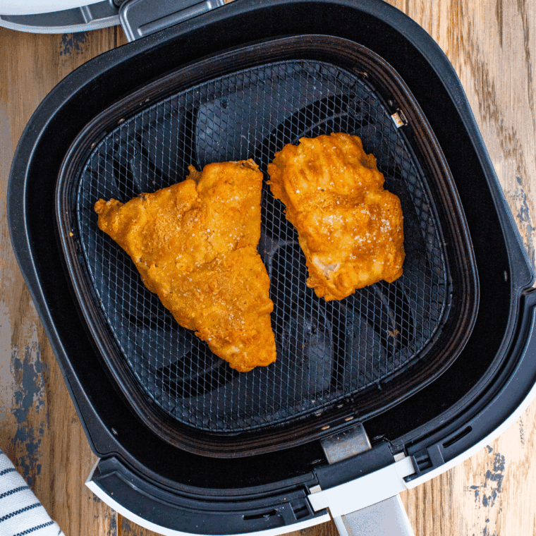 Placing breaded fish fillets in air fryer basket sprayed with cooking spray.