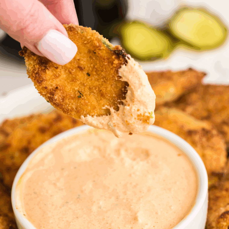 Golden-brown Arthur Treacher’s fried pickles served with dipping sauce on a white plate.