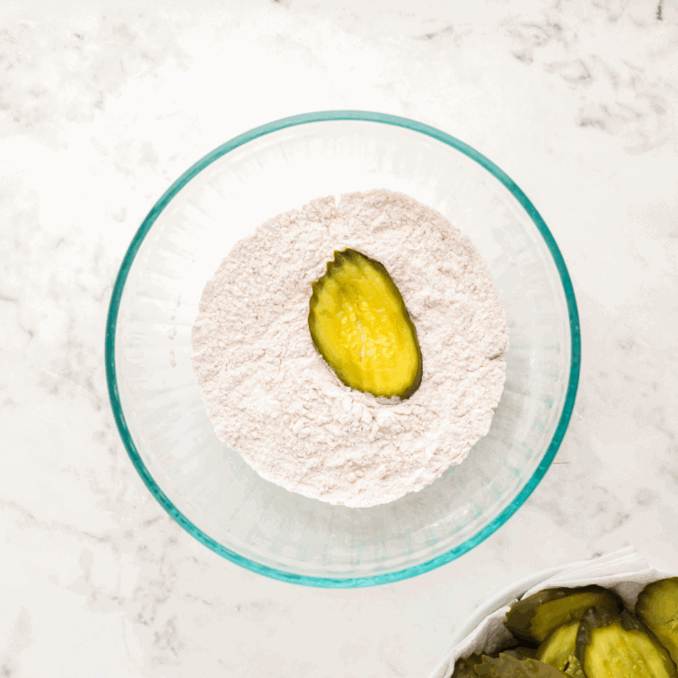 Pickle slices being coated in seasoned flour mixture in a bowl.
