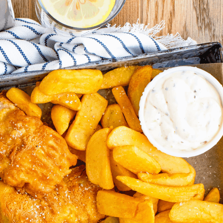 Homemade Arthur Treacher’s tartar sauce in a white bowl with a spoon, served next to crispy fried fish and golden fries.
