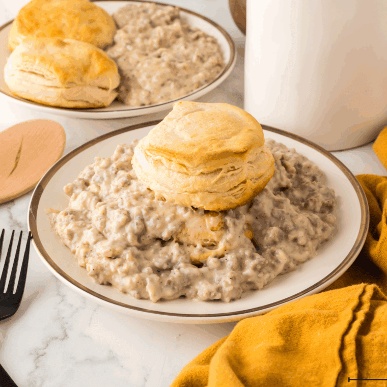 Golden brown Bob Evans style buttermilk biscuits stacked on a white plate with a pat of melting butter on top.
