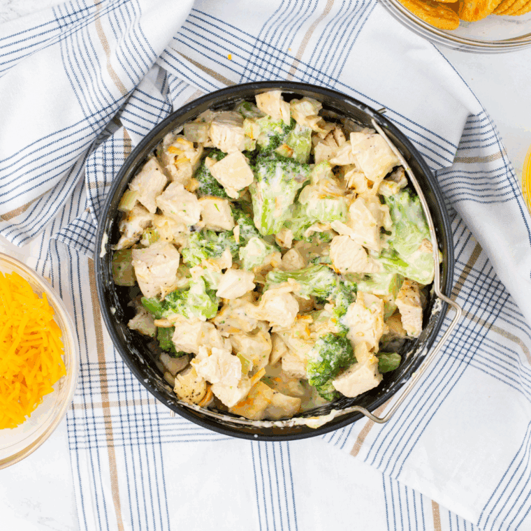 Folding shredded cooked chicken and steamed broccoli into the creamy sauce; spreading mixture evenly in the baking dish; topping with shredded sharp cheddar cheese.