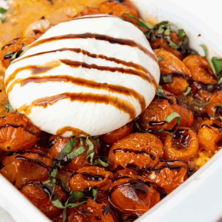 Fresh Carrabba’s Tomato Caprese with burrata, basil, and balsamic glaze on a white plate.