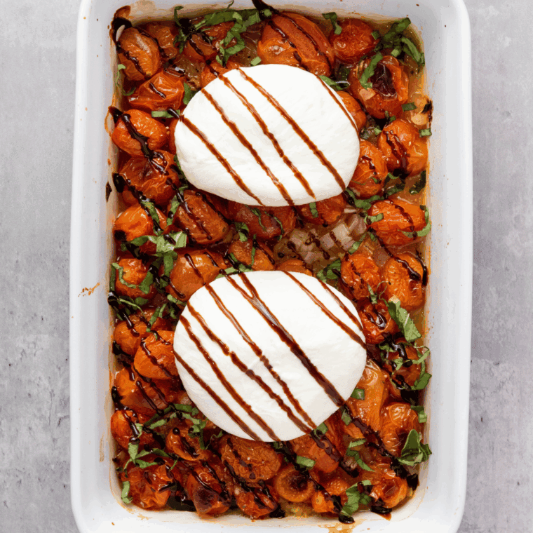 Burrata placed on roasted tomatoes with fresh basil on top.