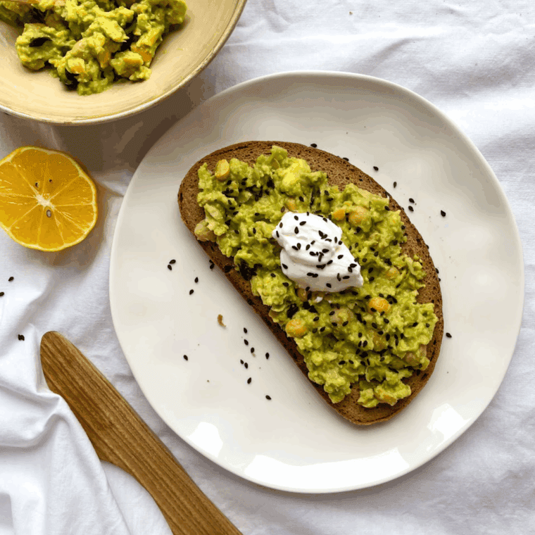 Cheesecake Factory-style avocado toast with mashed avocado, cherry tomatoes, and microgreens on toasted sourdough bread.