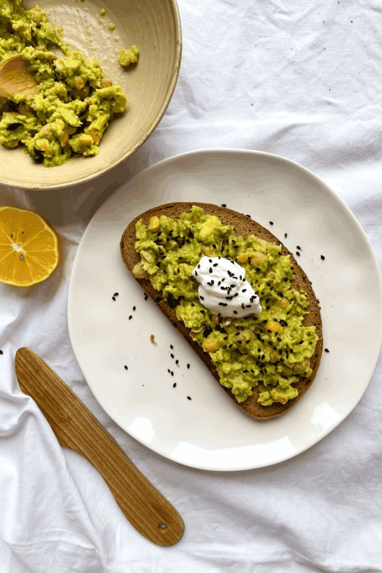 Close-up of Cheesecake Factory-style avocado toast with mashed avocado, cherry tomatoes, and microgreens on toasted sourdough bread.