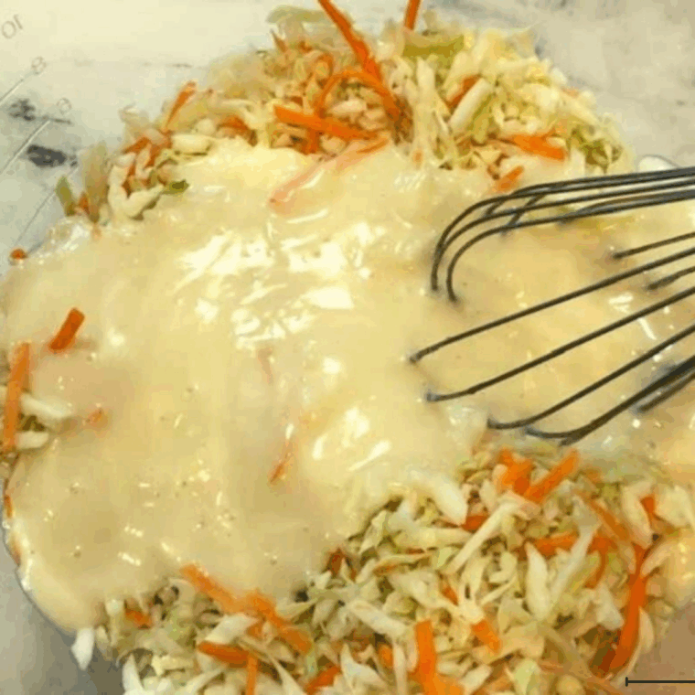 Pouring creamy dressing over shredded cabbage and carrots, tossing to coat.