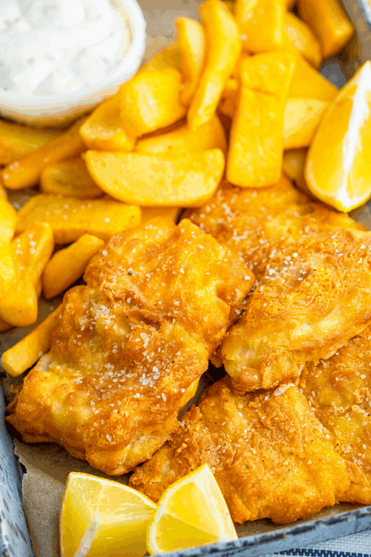 Golden crispy battered fish served on a plate with lemon wedges and dipping sauce.