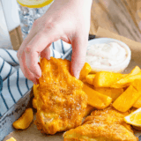 Golden crispy battered fish served on a plate with lemon wedges and dipping sauce.