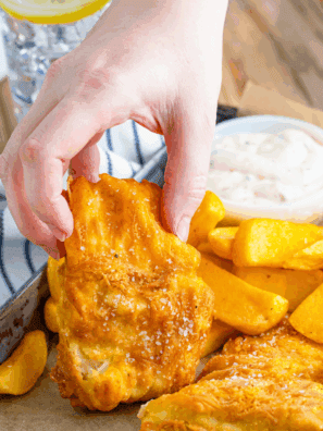 Golden crispy battered fish served on a plate with lemon wedges and dipping sauce.