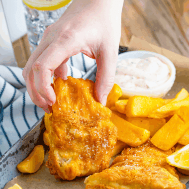 Golden crispy battered fish served on a plate with lemon wedges and dipping sauce.