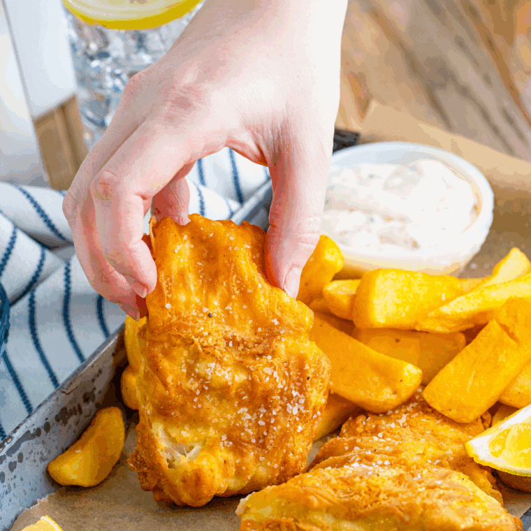 Crispy golden battered fish served on a plate with lemon wedges and dipping sauce.