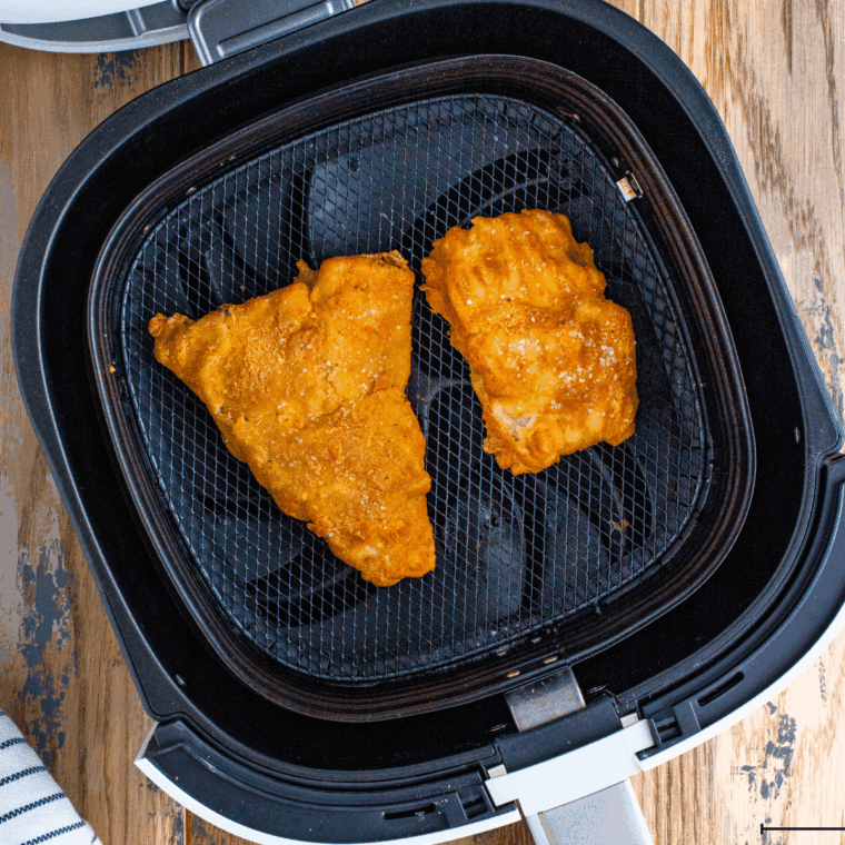 Coated fish fillets arranged in air fryer basket, sprayed with cooking spray, cooking to golden brown and crispy.