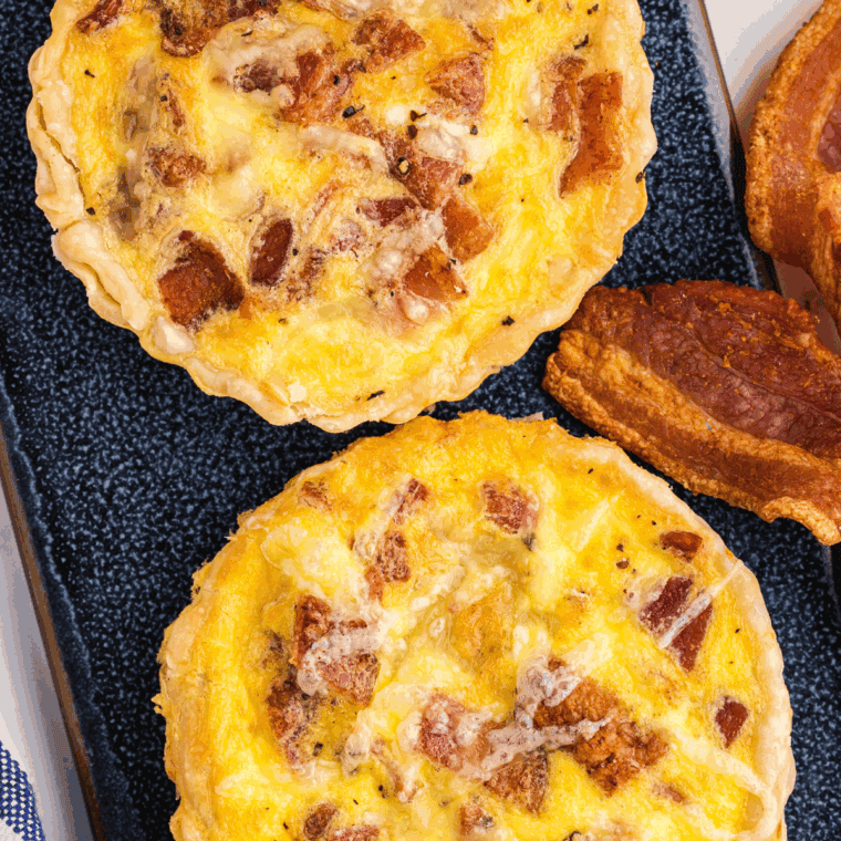 Homemade Cracker Barrel bacon and cheddar quiche with golden crust, melted cheese, and crispy bacon slices, served warm on a plate.