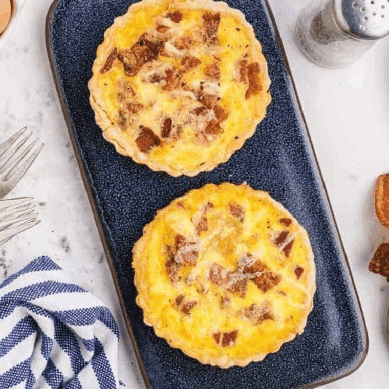 Golden-brown slice of Cracker Barrel-style bacon and cheddar quiche served on a plate with fresh herbs.