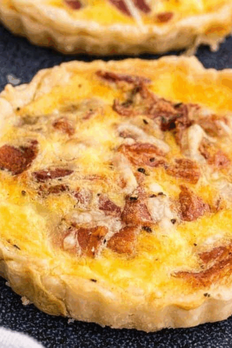 Golden-brown slice of Cracker Barrel-style bacon and cheddar quiche served on a plate with fresh herbs.