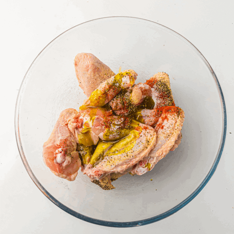 Chicken wings in a large bowl tossed with spices and olive oil, evenly coated and ready for cooking