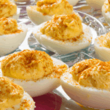 Deviled duck eggs topped with smoked paprika and fresh herbs on a serving platter.