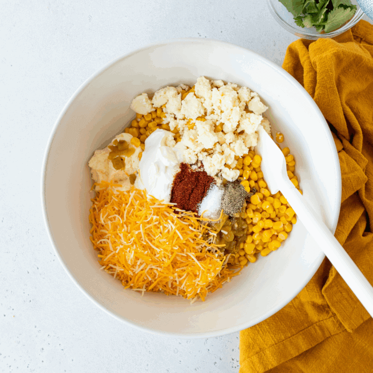 Mixing bowl with corn, mayonnaise, sour cream, chili powder, smoked paprika, salt, and pepper, evenly coated and ready for baking.