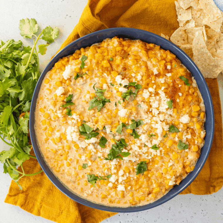 Baked Mexican Street Corn Casserole with melted cheese, chili powder, lime, and fresh cilantro in a serving dish.