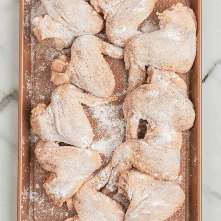 Chicken wings tossed with baking powder and salt in a glass bowl