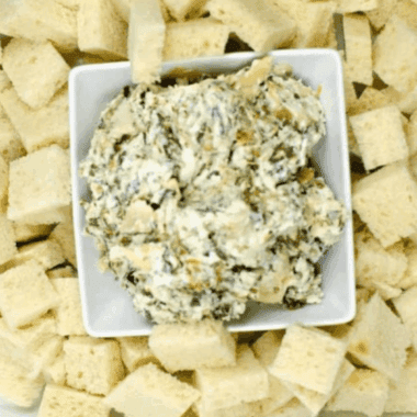 Baked Ina Garten Spinach Artichoke Dip in a white dish, hot and bubbly with golden cheese on top.